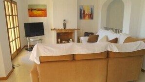 A living room with a large sofa, a TV, and artwork on the walls. -  Luxury Air Conditioned Villa Close to Calonge Centre - Fantastic Views (Calonge)