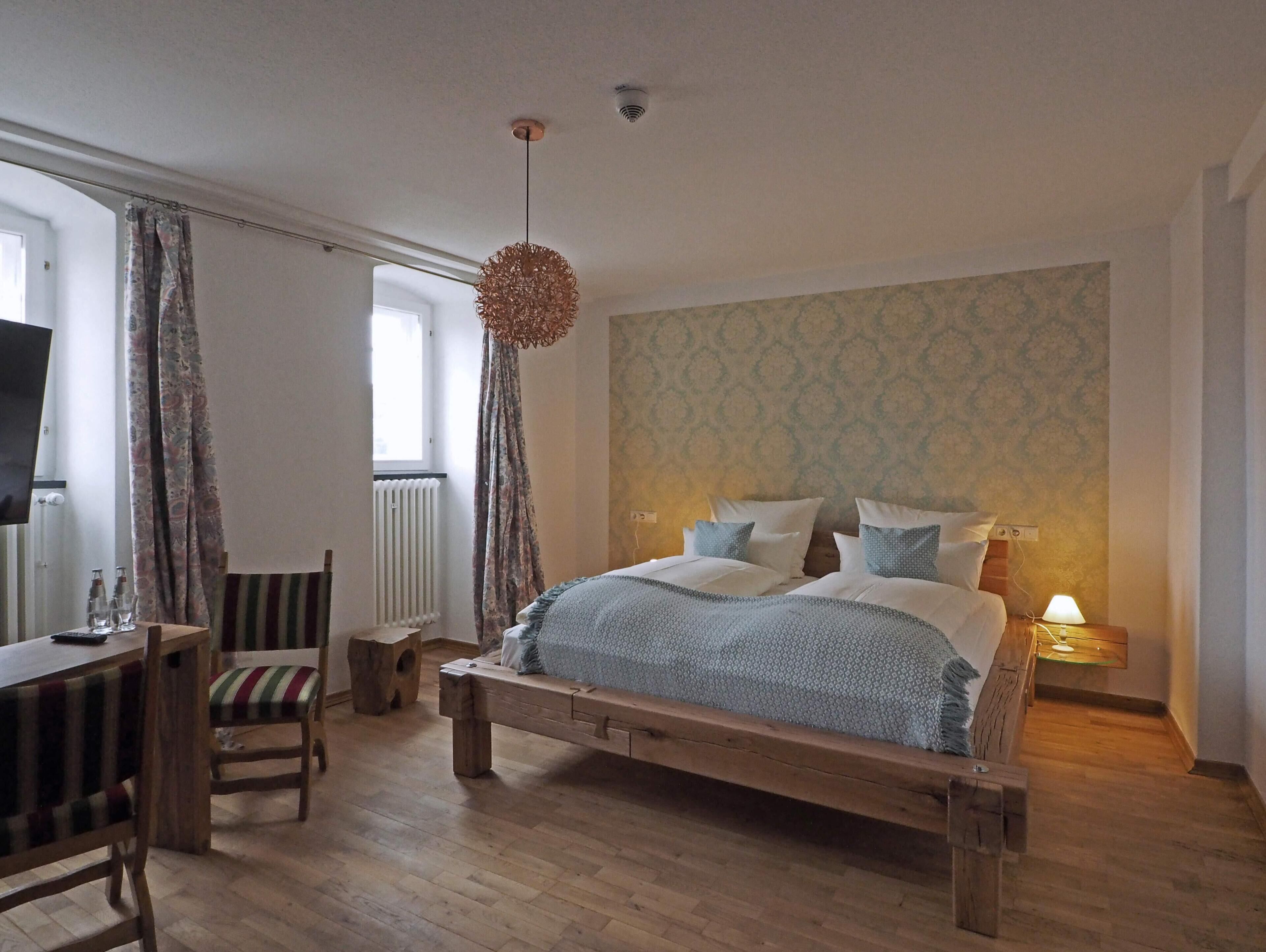 A bedroom with a wooden bed, a desk with chairs, a television, and a patterned wall.