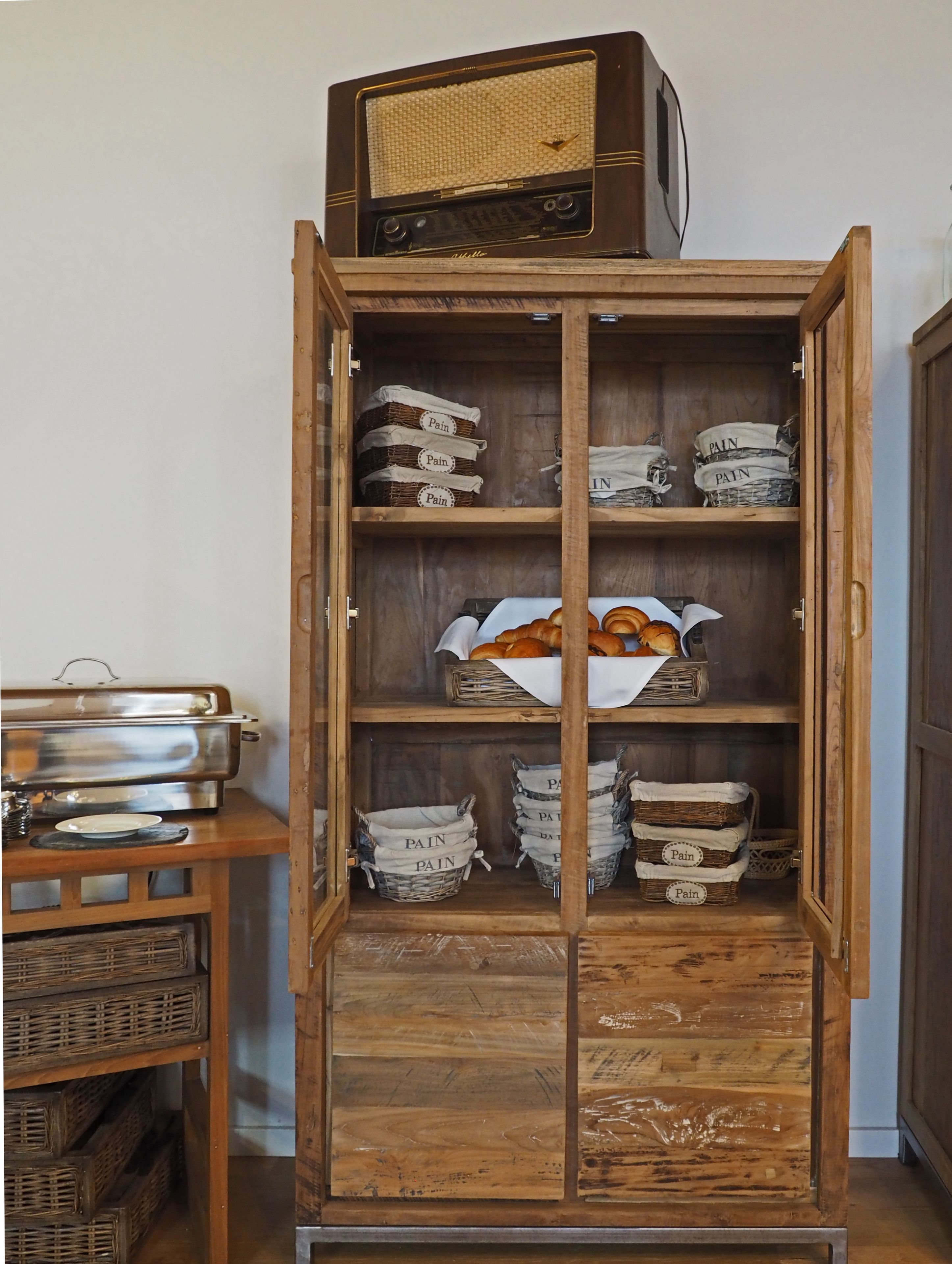 Un mueble de madera con varios estantes, algunos con cestas etiquetadas “PAIN” y una radio antigua en la parte superior.