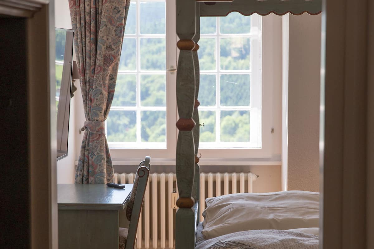 A bedroom with a wooden four-poster bed, a desk, and a chair.