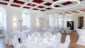 A banquet hall with round tables set for a formal event, white chairs, and chandeliers.