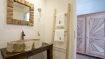 Ein Badezimmer mit einem Steinkonstruktion-Waschbecken, einem Holztischchen, einem hölzernen Handtuchhalter und einer Holztür mit Sonnenscheibendesign.