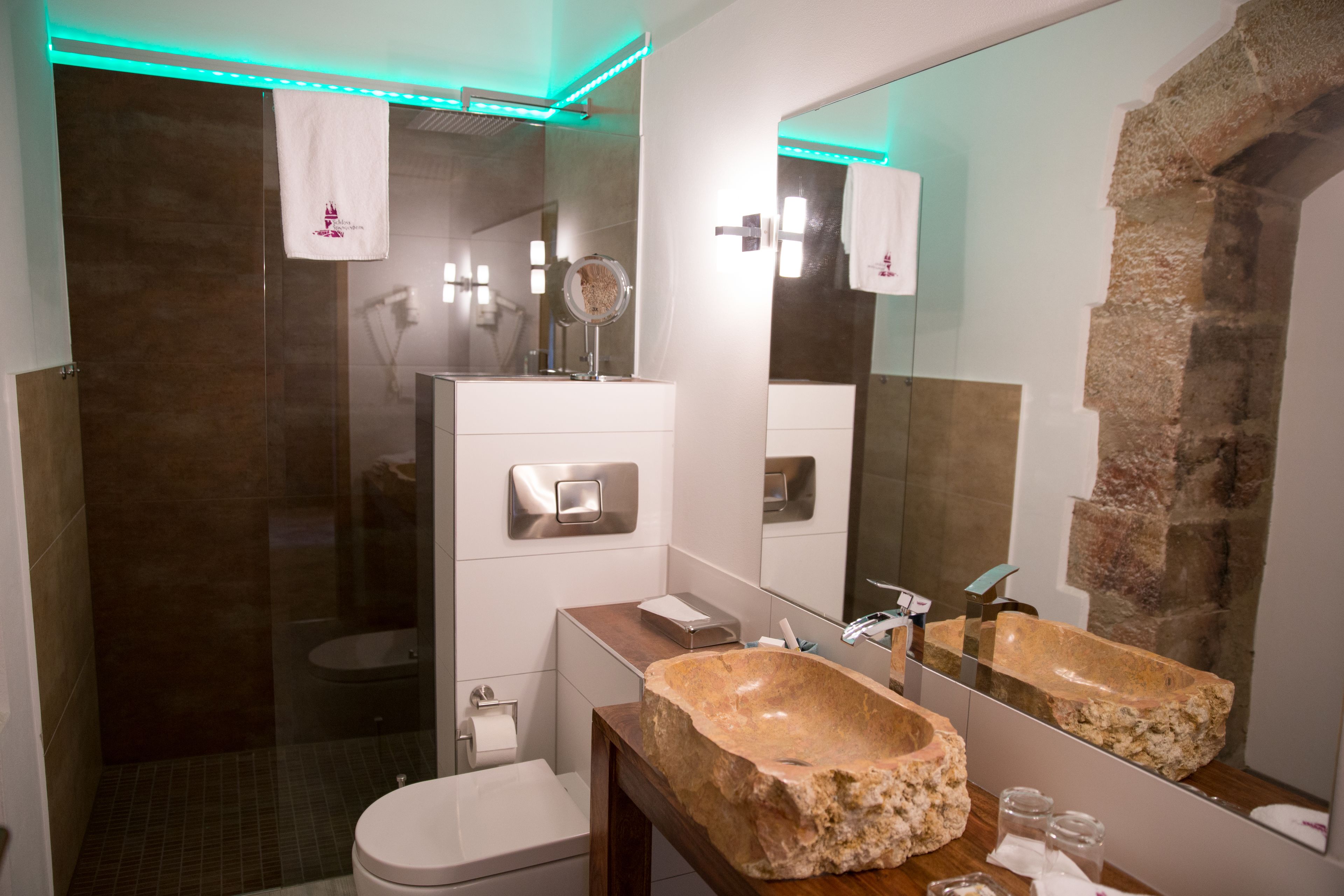 Une salle de bain moderne avec un grand miroir, un lavabo en pierre et une douche à parois de verre.