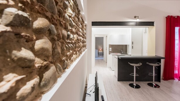 Una cocina moderna con una pared de acento de piedra, una barra con taburetes y un sendero visible que conduce a un comedor.