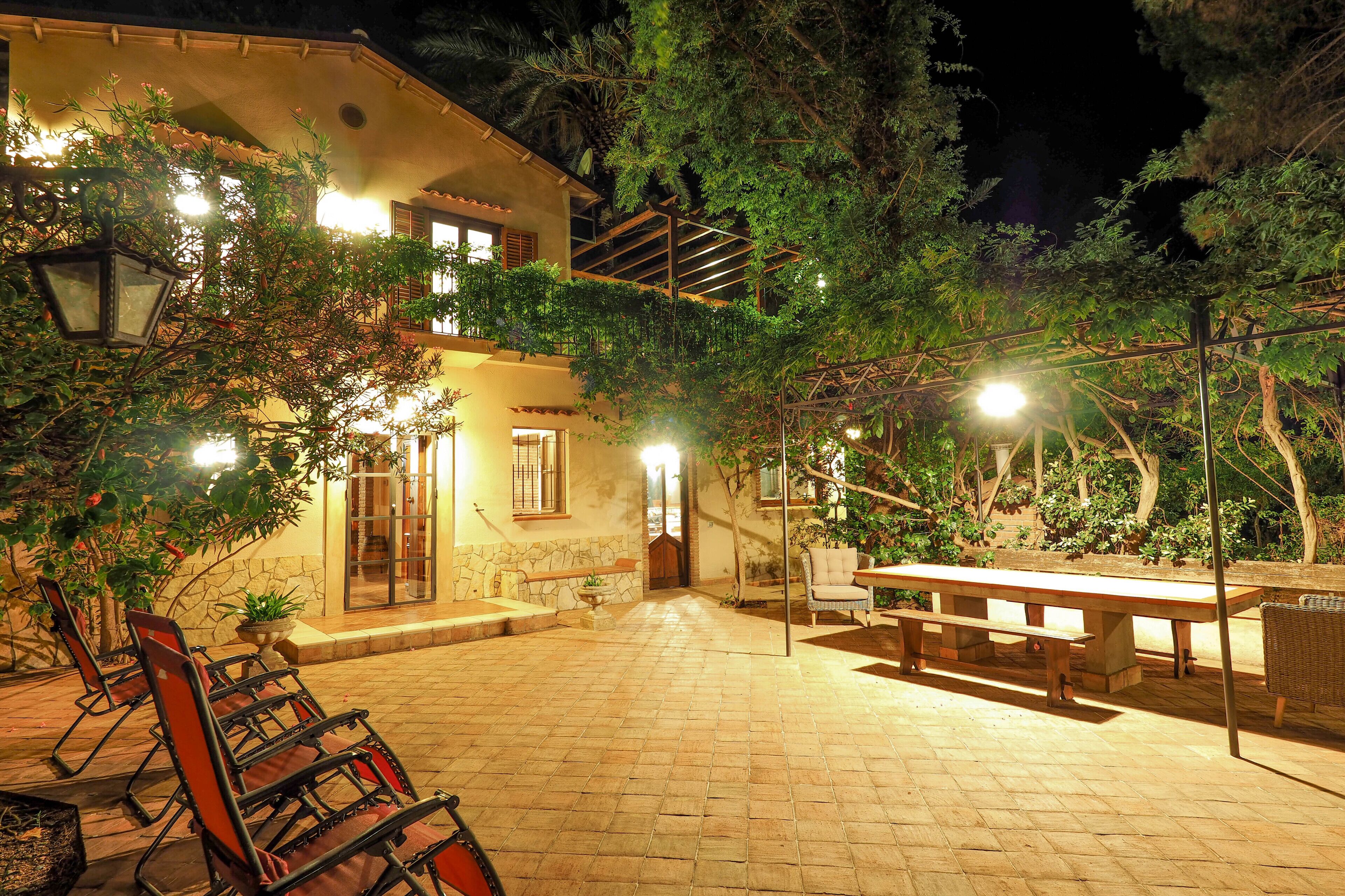 An outdoor patio area with a stone floor, wooden benches, and tables. There are chairs and a lamp post.