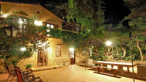 An outdoor patio area with a stone floor, wooden benches, and tables. There are chairs and a lamp post.