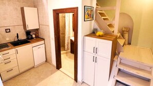 Una cucina con mobili bianchi, un piano di lavoro in legno e un piano cottura integrato. Si vede una scala con ringhiera in legno che conduce a un livello superiore.
