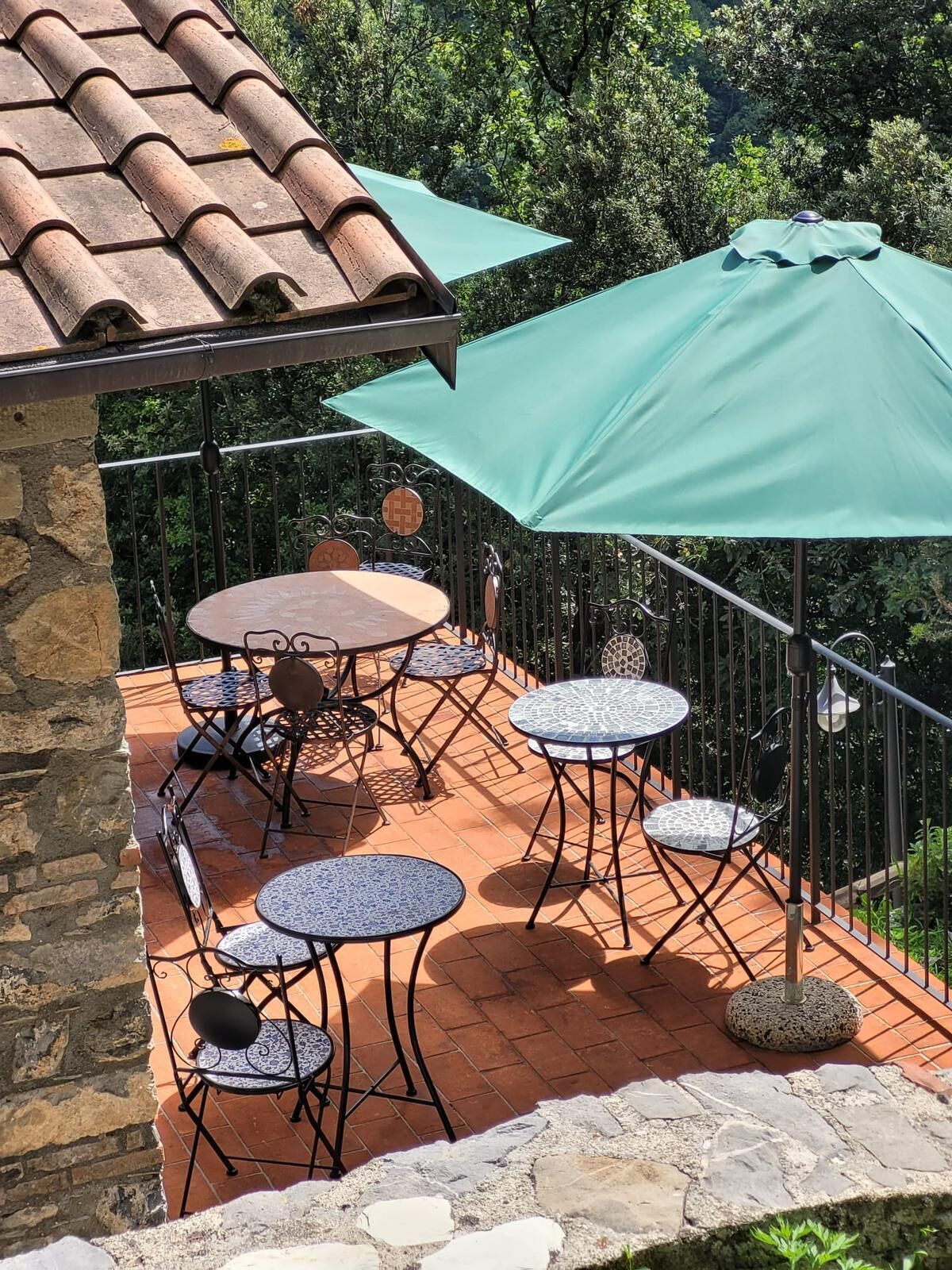 A terrace with a stone wall, a tiled roof, and a green umbrella providing shade.