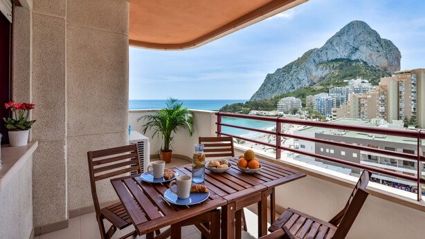 A balcony with a table set for breakfast, overlooking a coastal city and a prominent mountain. - Zafiro 18B - Front line apartment with sea views and direct access to the beach (Calpe / Calp)