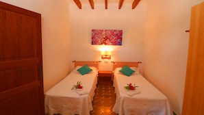 Une chambre avec deux lits simples, une porte en bois, un tableau au mur et une table de chevet avec une lampe.