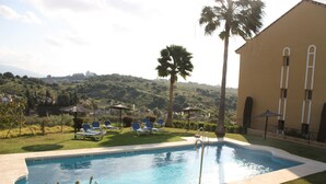 A swimming pool with lounge chairs, a palm tree, and a building with arched windows.