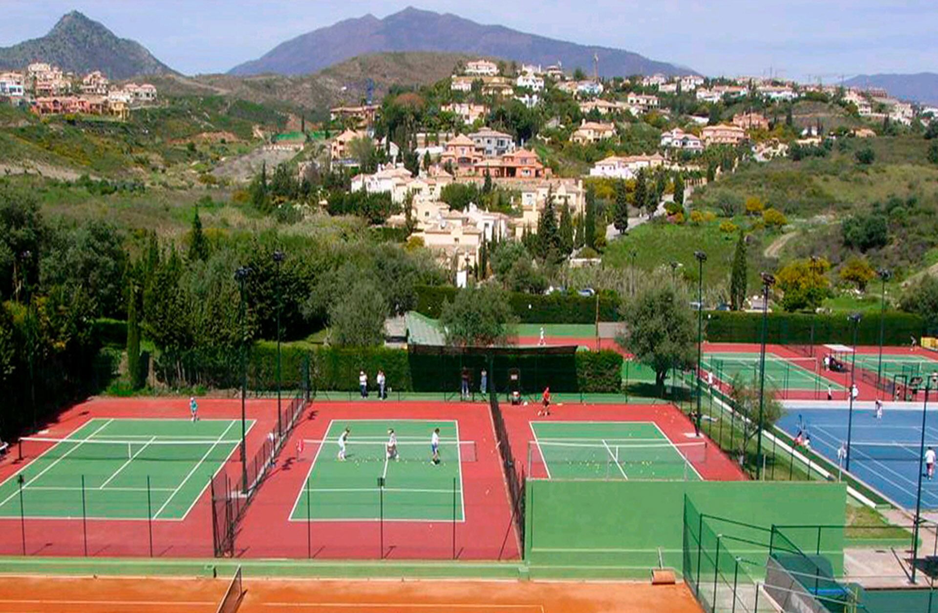 A tennis court complex with multiple courts, surrounded by residential buildings and greenery.