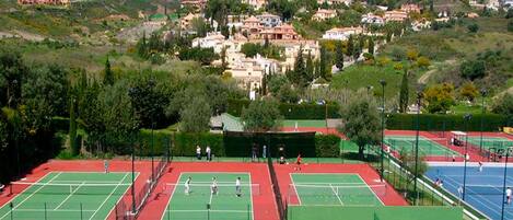 A tennis court complex with multiple courts, surrounded by residential buildings and greenery.