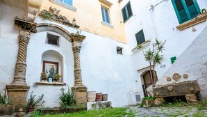 Un patio con senderos adoquinados, una estatua y un edificio de fachada blanca y contraventanas verdes.