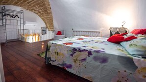 Un dormitorio con suelo de madera, una cama con colcha estampada, un almohadón rojo y un arco de ladrillo.