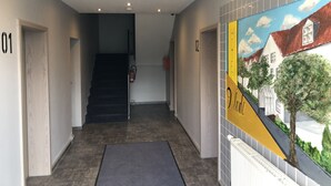 A hotel hallway with a staircase, numbered doors, and a mural of a street scene. - Hotel Vladi (Walldorf)