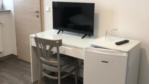 A small, neatly arranged room with a white desk, a chair, a television, and a compact refrigerator. - Hotel Vladi (Walldorf)