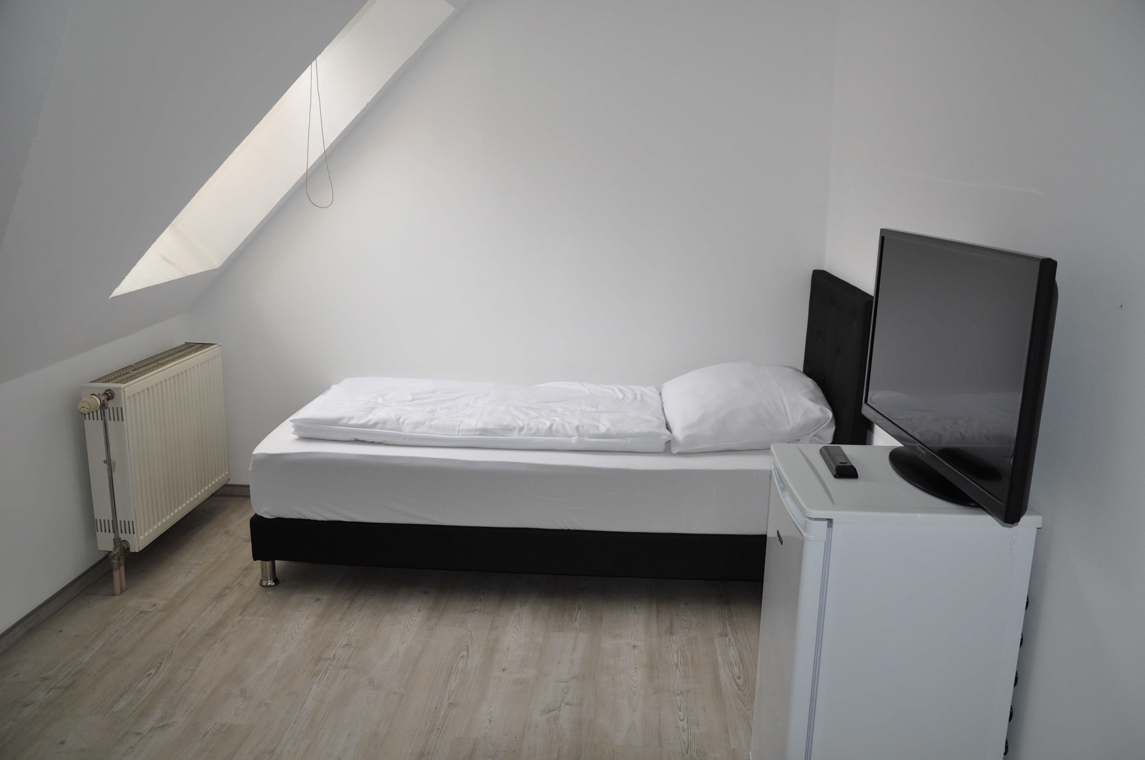 A small, modern bedroom with a single bed, a television on a stand, and a skylight above.