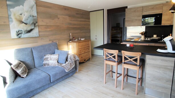 A modern kitchen with wooden cabinets, a dining area with a blue sofa and two wooden chairs, and a large polar bear painting on the wall. - LES 2 ALPES .. RENTED APARTMENT WITHOUT OPPOSITE (Mont-de-Lans)