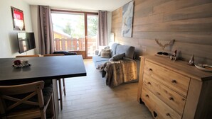 A room with a wooden floor, a sofa, a wooden dresser, a television on the wall, and a dining table with chairs. - LES 2 ALPES .. RENTED APARTMENT WITHOUT OPPOSITE (Mont-de-Lans)