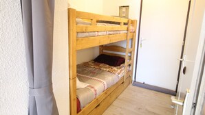 A bunk bed with a wooden frame, a mattress with a patterned blanket, and a door with a handle. - LES 2 ALPES .. RENTED APARTMENT WITHOUT OPPOSITE (Mont-de-Lans)