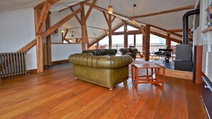 A spacious loft with exposed wooden beams, a leather sofa, and a dining area with a table and chairs. - Chalet 3 Valleys France (Saint-Jean-De-Belleville)