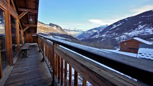 A wooden deck with a view of snow-covered mountains and a cabin. - Chalet 3 Valleys France (Saint-Jean-De-Belleville)