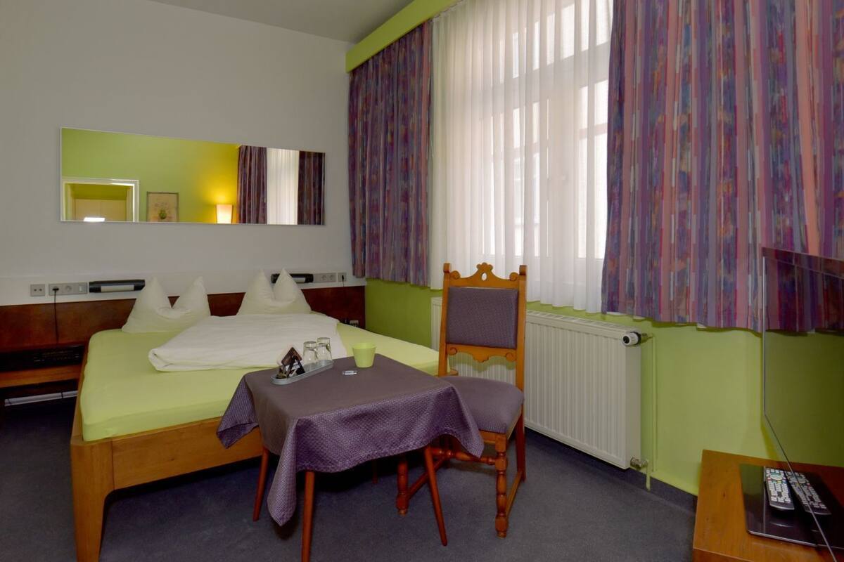 Een hotelkamer met een bed, een stoel, een tafel, een spiegel en een televisie.