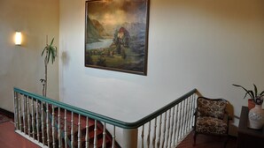 Un escalier avec une rampe, un tableau représentant un paysage et une chaise.
