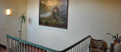 A staircase with a railing, a painting of a landscape, and a chair.