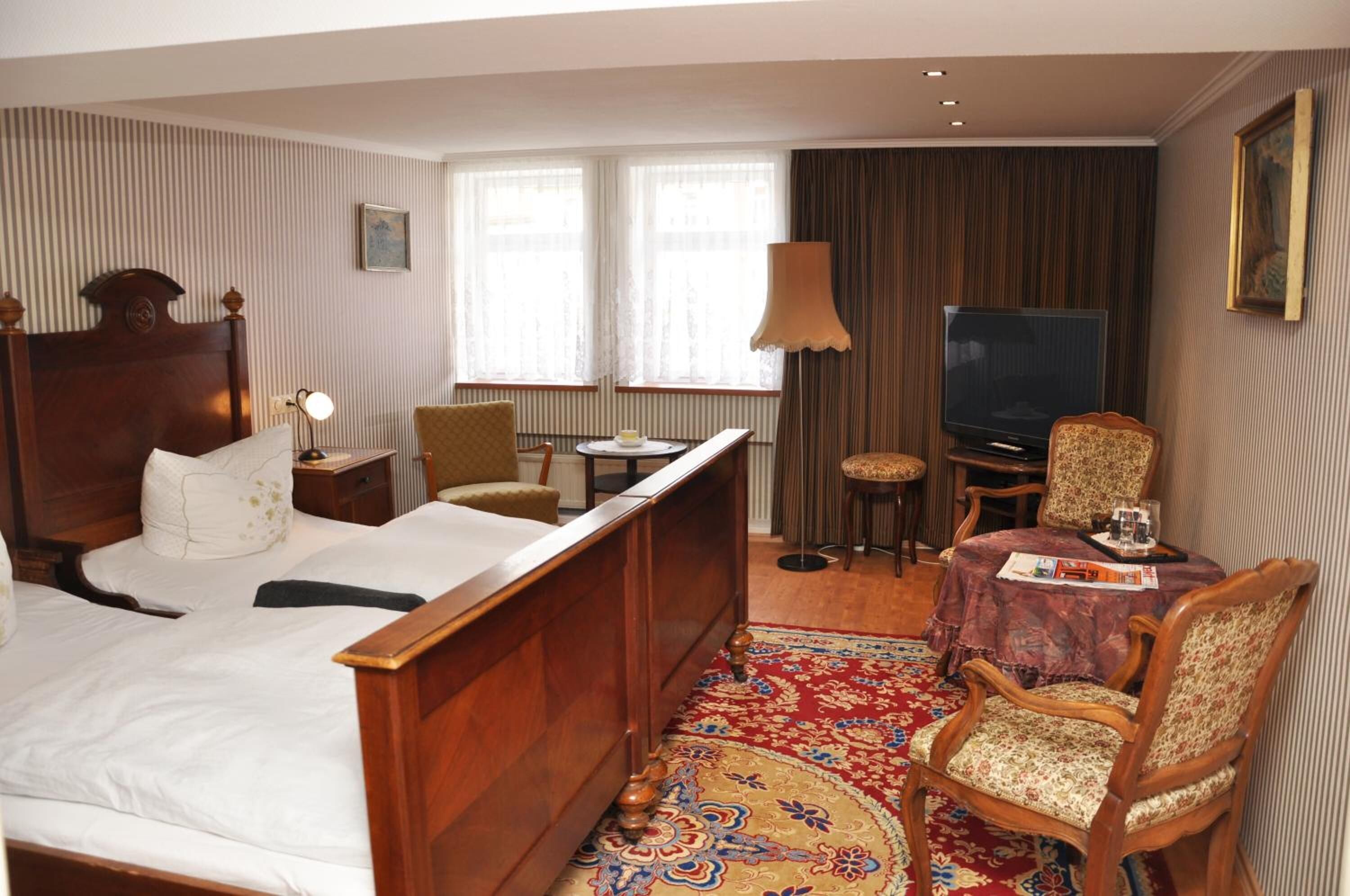 Ein Hotelzimmer mit einem hölzernen Bett, einem Fernseher, einem Esstisch mit Stühlen und einem gemusterten Teppich.