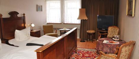 Una habitación de hotel con una cama de madera, televisión, una mesa de comedor con sillas y una alfombra estampada.