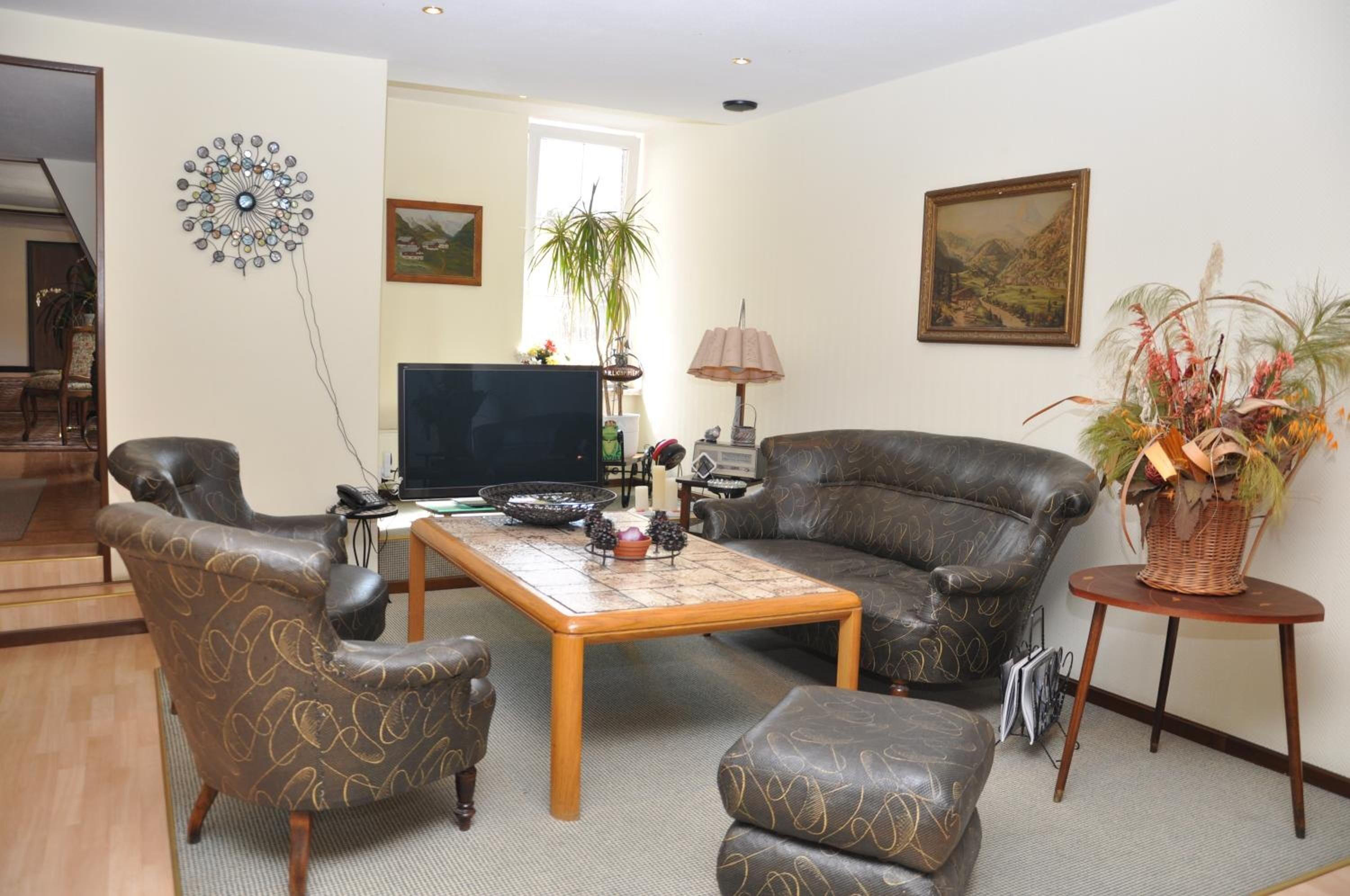 Ein Wohnzimmer mit einer Couch, Sesseln, einem Couchtisch, einem Fernseher und Dekorationselementen.
