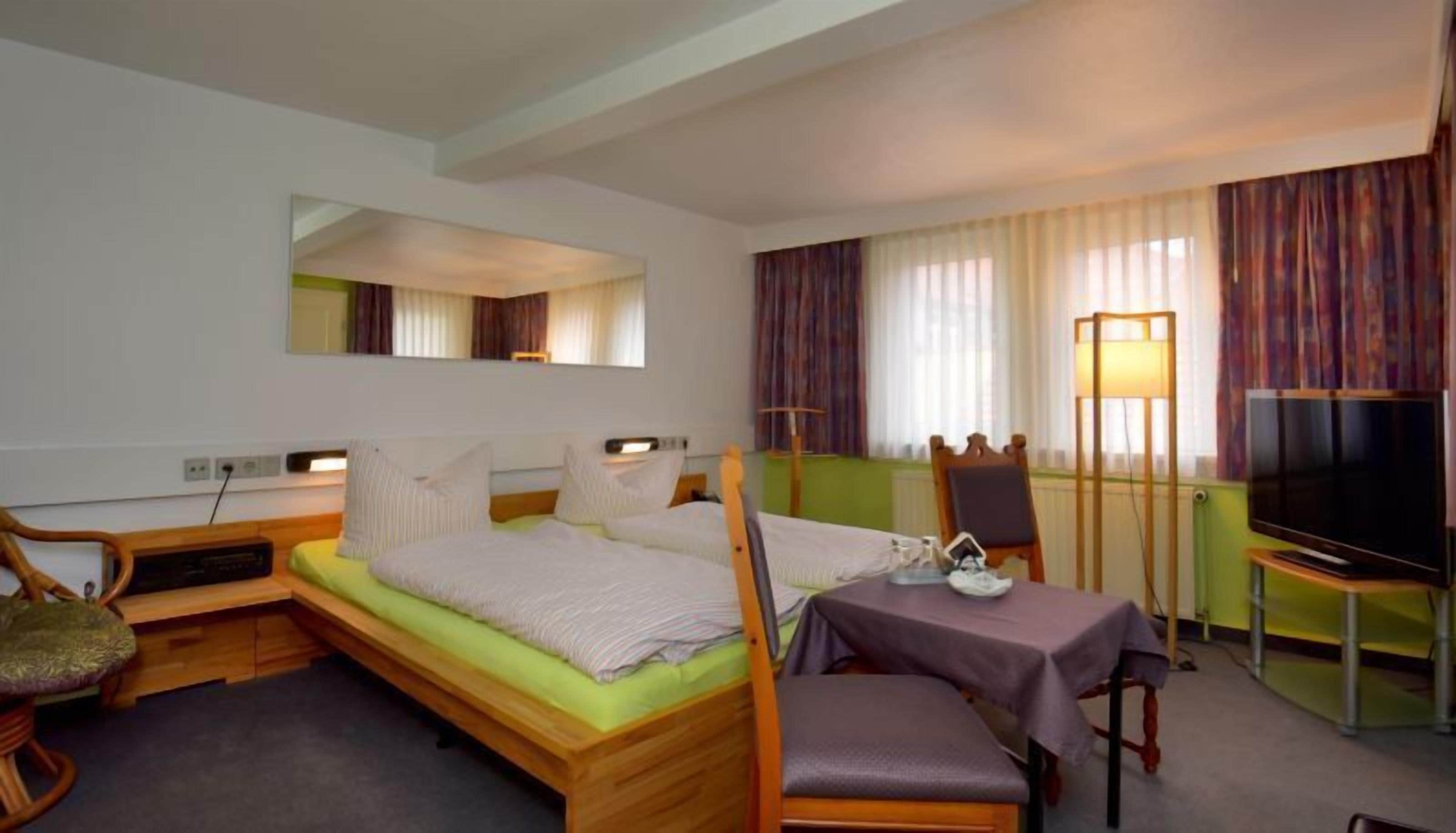 A hotel room with a bed, a desk, a chair, a television, and a mirror.