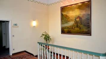 A hallway with a painting of a landscape, a staircase with a railing, and a potted plant.