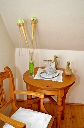 A wooden dining table with a placemat, a glass vase with green decorative items, two decorative sticks, and a small bird figurine.
