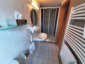 A bathroom with a glass shelf, a sink, a mirror, a shower, and a towel rack.