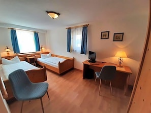 A hotel room with two beds, a desk with a computer, a chair, and a television.