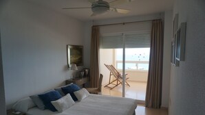 A hotel room with a bed, a desk, a chair, a ceiling fan, and a view of the outside balcony.