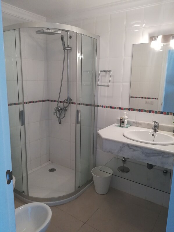 A modern bathroom with a glass-enclosed shower, a white sink with a marble countertop, and a large mirror.