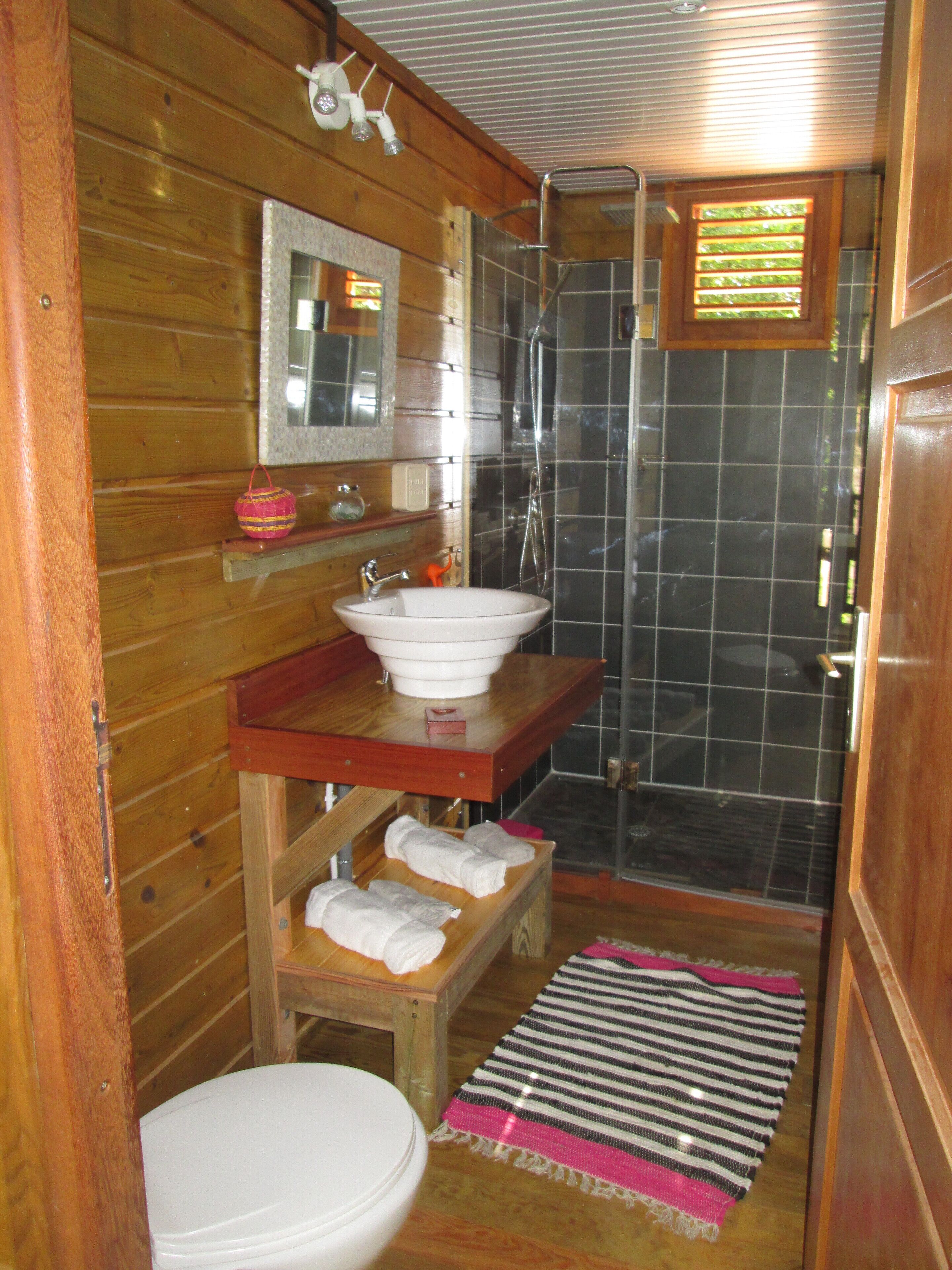 A wooden cabin bathroom with a white sink, mirror, and shower.