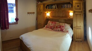 Une chambre confortable avec une tête de lit en bois, un lit avec une literie blanche et rouge, et une bibliothèque remplie de livres et ornée d’un objet décoratif en forme de cœur.