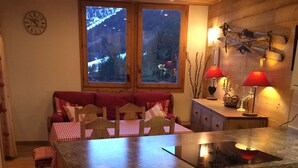 Une cuisine chaleureuse avec des meubles en bois, un coin repas avec une nappe à carreaux rouges et blancs, et une vue sur un paysage enneigé par les fenêtres.