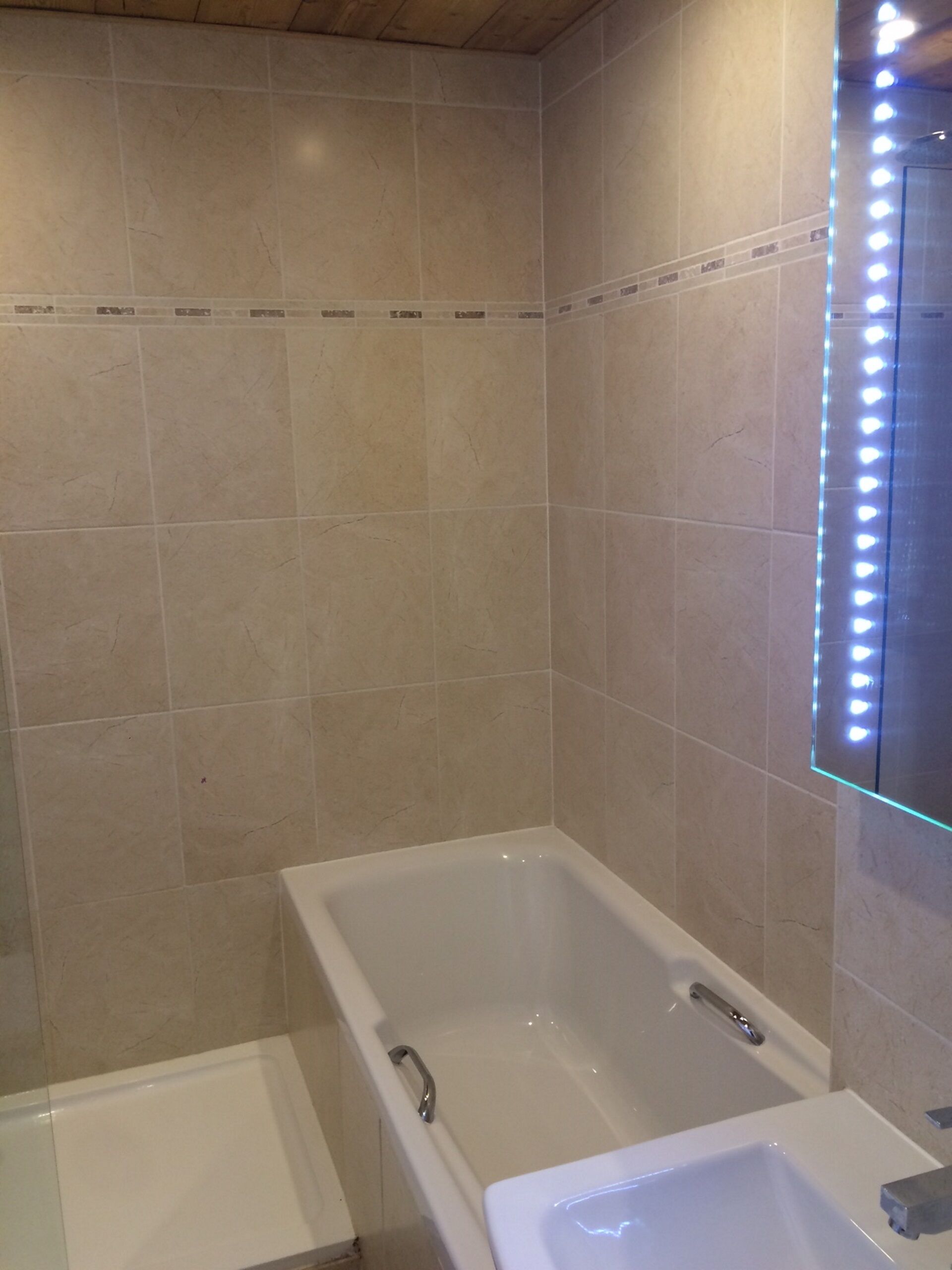 Un baño con bañera, lavabo e iluminación LED en el espejo.