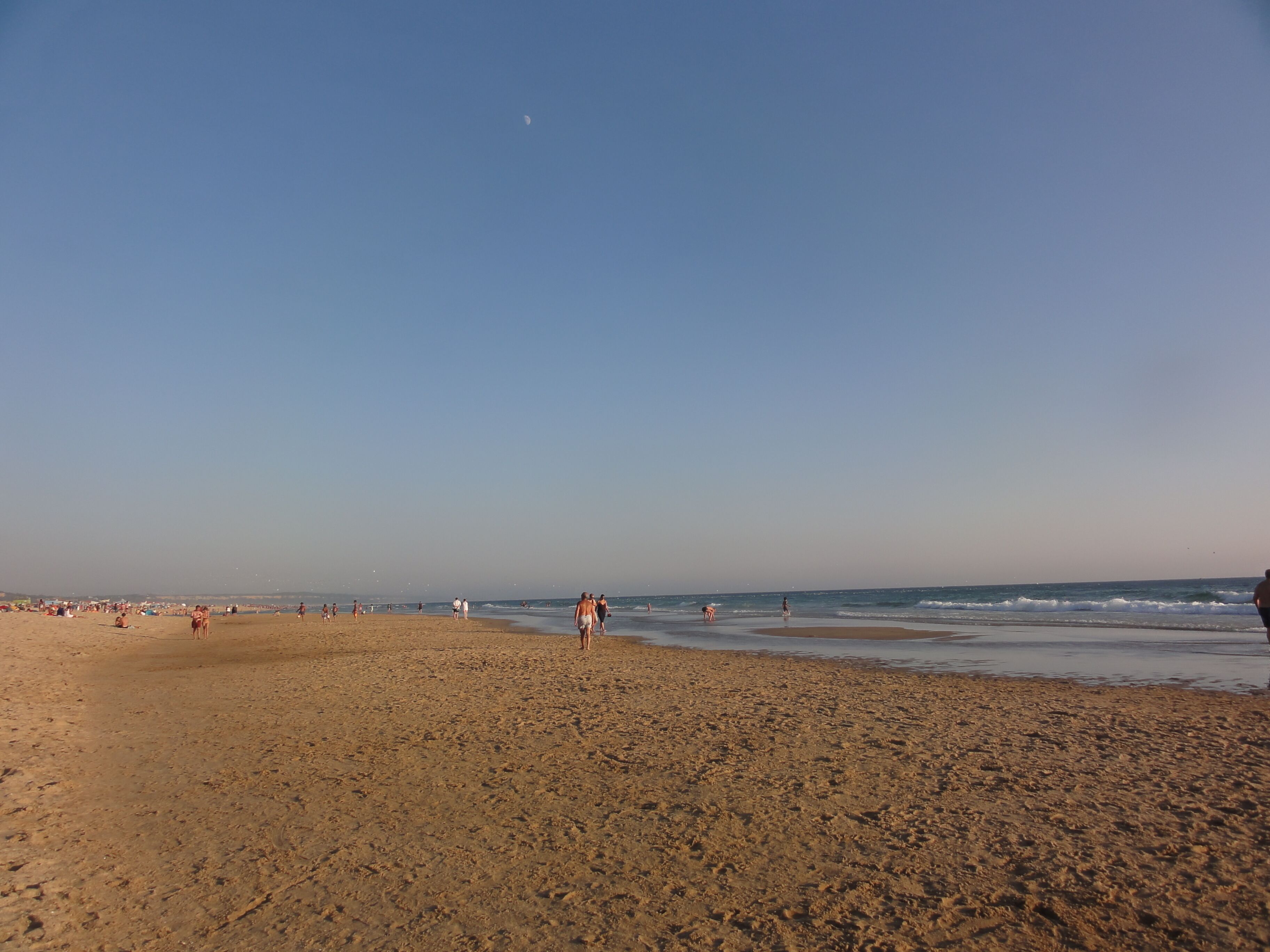 Uma extensa praia de areia com pessoas caminhando e paradas.