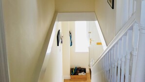 Un pasillo con un cartel de Cornualles, una escalera con barandillas blancas y una puerta al final.