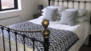 Una cama bien tendida con un edredón estampado, una lámpara de noche y un cuadro en la pared.