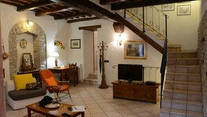 A living room with a stone archway, a sofa, a television, a wooden coffee table, and a staircase with a wrought iron railing. - CASA LA TORRE in the small Umbrian village of Macerino (Acquasparta)