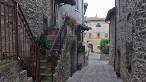 A narrow cobblestone street flanked by stone buildings with balconies and potted plants. - CASA LA TORRE in the small Umbrian village of Macerino (Acquasparta)