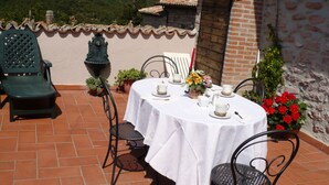 A terrace with a table set for four, surrounded by chairs, potted plants, and a view of hills. - CASA LA TORRE in the small Umbrian village of Macerino (Acquasparta)